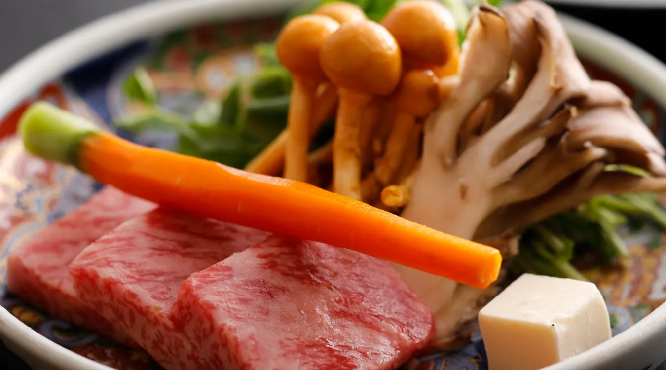 花纹瓷盘内盛放着雪花纹理牛肉、橙色胡萝卜、棕色菌菇与豆腐块。