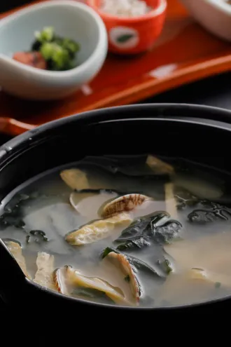 黒い漆器に注がれた、あさりとわかめの温かいお味噌汁。