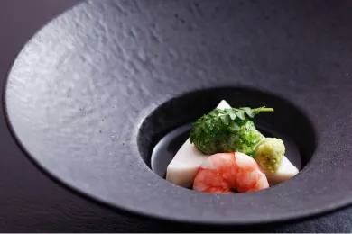 黒い深皿に盛り付けられた、海老や旬の食材を使った繊細な一品。