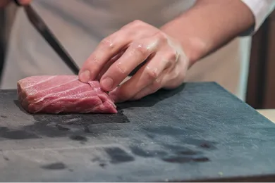 黒いまな板の上で、料理人が丁寧に包丁を入れる手元。