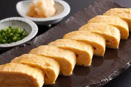 黒の長皿に盛られたふっくらとしただし巻き玉子、大根おろしと刻みネギ添え。