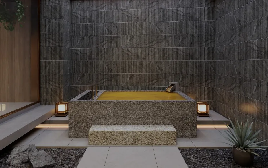 Atmospheric open-air bath with golden hot spring water pouring into a solid stone tub, framed by dark grey stone walls and lantern lighting.