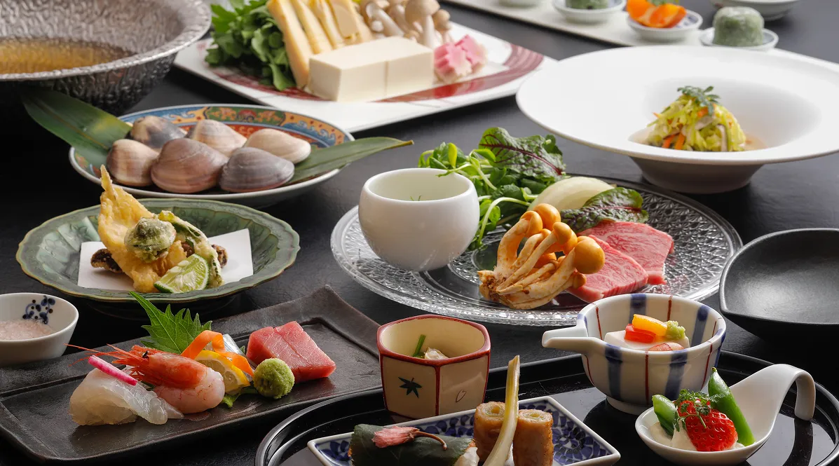 彩り豊かな和洋懐石の料理が一揃い並ぶ食卓。手前に鮮やかなお刺身や前菜の小鉢、中央に黒毛和牛とキノコ、奥にはお鍋の具材や天ぷらが並ぶ豪華な夕食の一例。